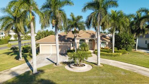 A two-story house with a garage, surrounded by palm trees and well-maintained lawns. - Waterfront, Private Pool, Close to Beaches, Best of Marco! (Marco Island)