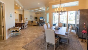A spacious living area with a dining table, chairs, a chandelier, and a large window providing a view of the outdoors. - Waterfront, Private Pool, Close to Beaches, Best of Marco! (Marco Island)