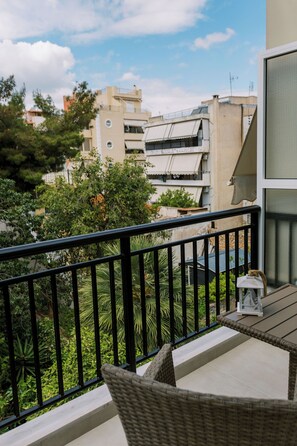Een balkon met een rieten stoel, een tafeltje en een kat.