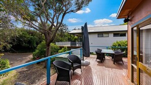 A wooden deck with outdoor furniture, a covered seating area, and a view of a house with a balcony. - The Lohr Shack - 150 metres from the Beach (Inverloch)