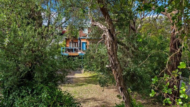 A pathway leading to a building with a blue and orange facade, surrounded by dense greenery. - The Lohr Shack - 150 metres from the Beach (Inverloch)