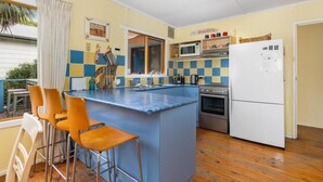 A compact kitchen with a central island, a microwave, a stove, and a refrigerator. There are bar stools and a small dining table. - The Lohr Shack - 150 metres from the Beach (Inverloch)