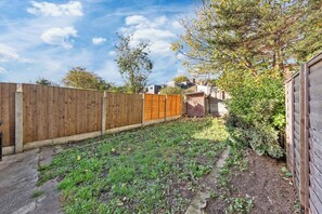 Un jardin avec une clôture en bois, un espace dédié à la plantation et un petit abri de jardin.