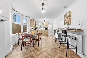 Une cuisine moderne avec un plancher en bois, un coin repas avec une table et des chaises en bois, et un îlot de cuisine avec des tabourets de bar.