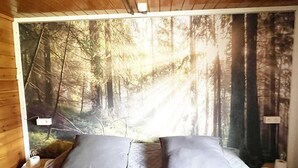 Un dormitorio con un gran mural de un bosque en la pared, una cama con ropa de cama gris y un techo de madera.