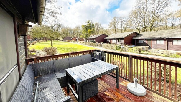 Una terraza con mesa y asientos, con vistas a un espacio verde con casas.