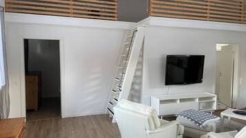 A modern living room with a white sofa, a TV mounted on the wall, and a wooden staircase.