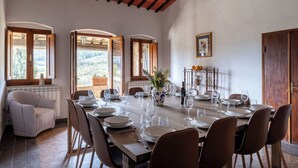 A dining area with a long table set for six, wooden chairs, a vase with flowers, and a fruit basket. - Podere le Lune with Pool, San Gimignano (San Gimignano)