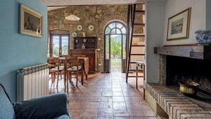 A rustic interior with a stone wall, a fireplace, a dining area with wooden chairs, and a view through an arched doorway. - Podere le Lune with Pool, San Gimignano (San Gimignano)