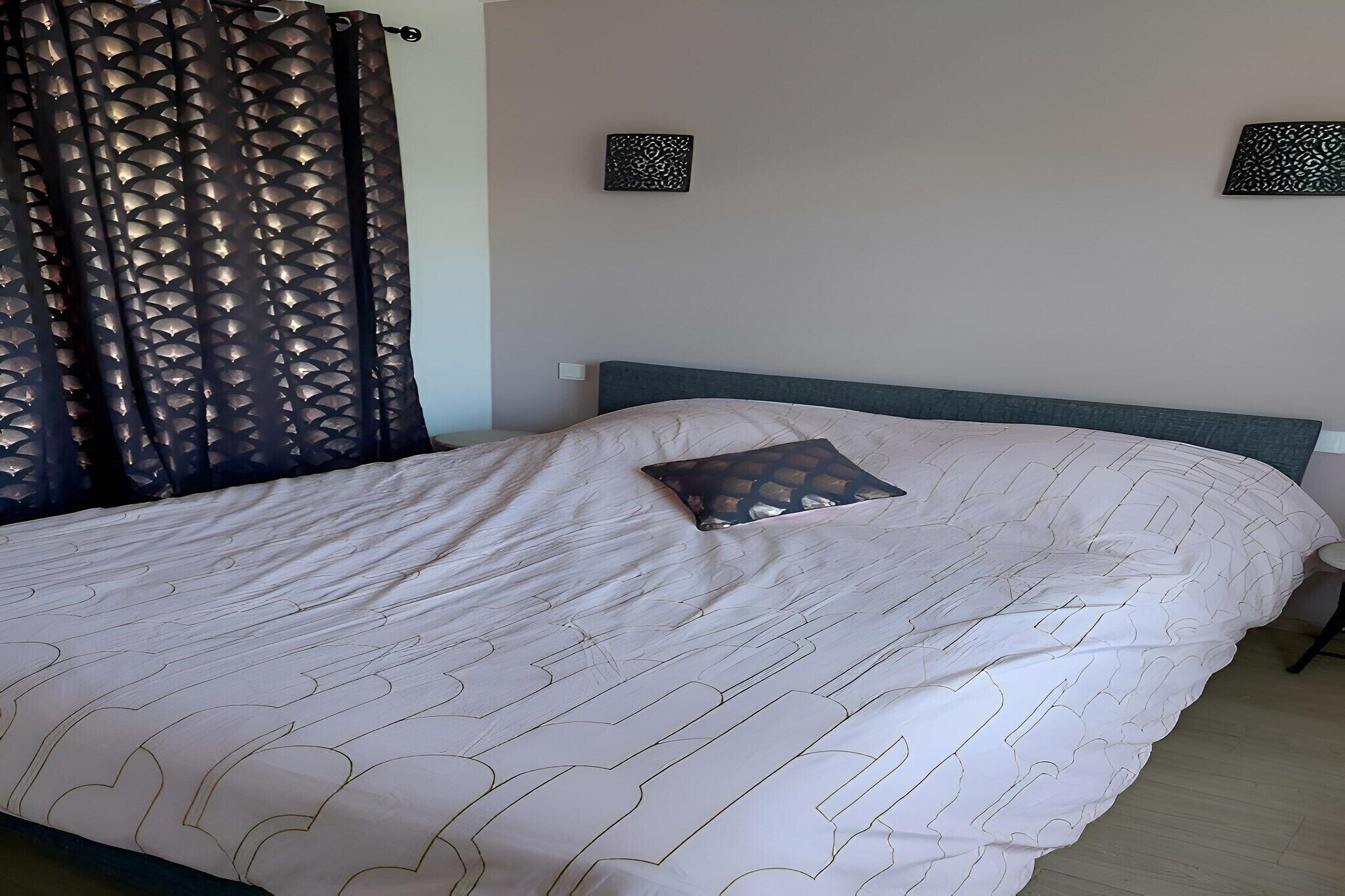 Un lit bien fait, avec une couvre-lit à motifs et un seul coussin décoratif.