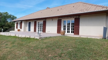 Une maison à deux étages, avec un toit en tuiles, de grandes fenêtres dotées de volets et un porche à l’avant.