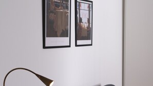 Ett modernt vardagsrum med en mörkgrå soffa, en golvlampa och två inramade fotografier på väggen.