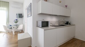 Ett modernt kök med vita köksskåp, en mikrovågsugn, en diskho och en matplats med ett glasbord och stolar.