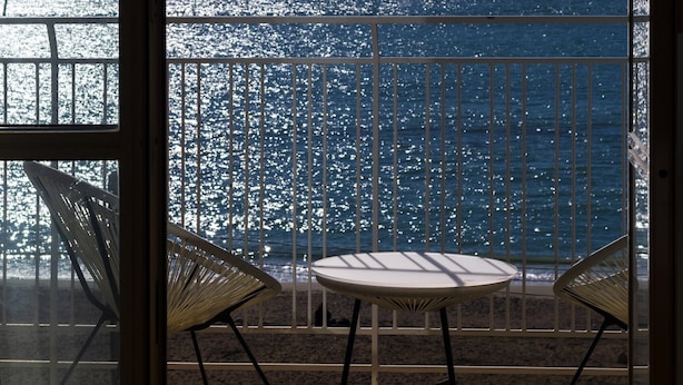 En balkong med utsikt över havet, två stolar och ett bord.