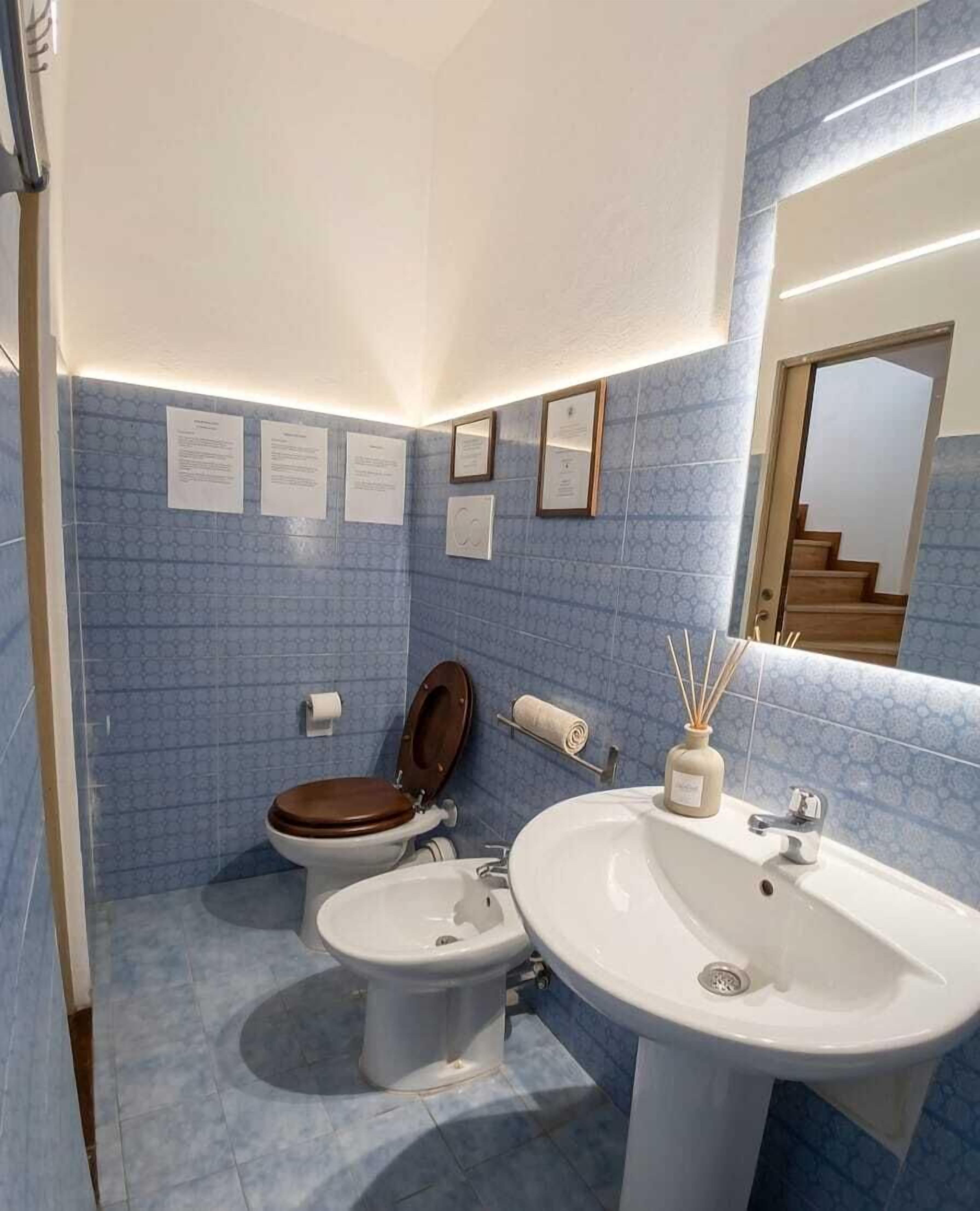 A bathroom with a toilet, bidet, and sink, blue tiled walls, and a mirror.