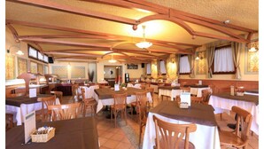 Un restaurante con vigas de madera, manteles blancos y cestas de mimbre sobre las mesas.