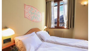 Una habitación de hotel con cama, mesita de noche con lámpara, ventana con cortinas y un adorno en la pared.