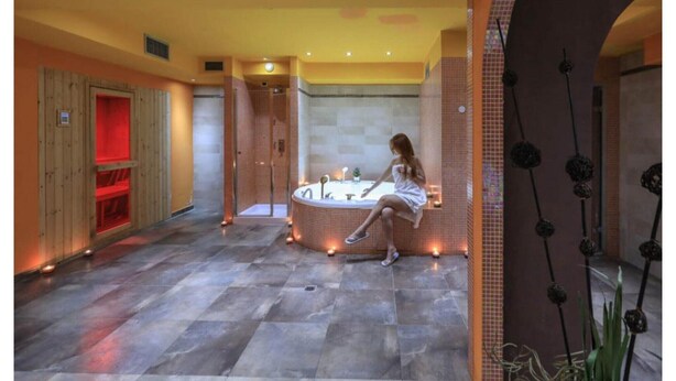Un área de spa con una bañera grande, sauna de madera y suelo de baldosas.