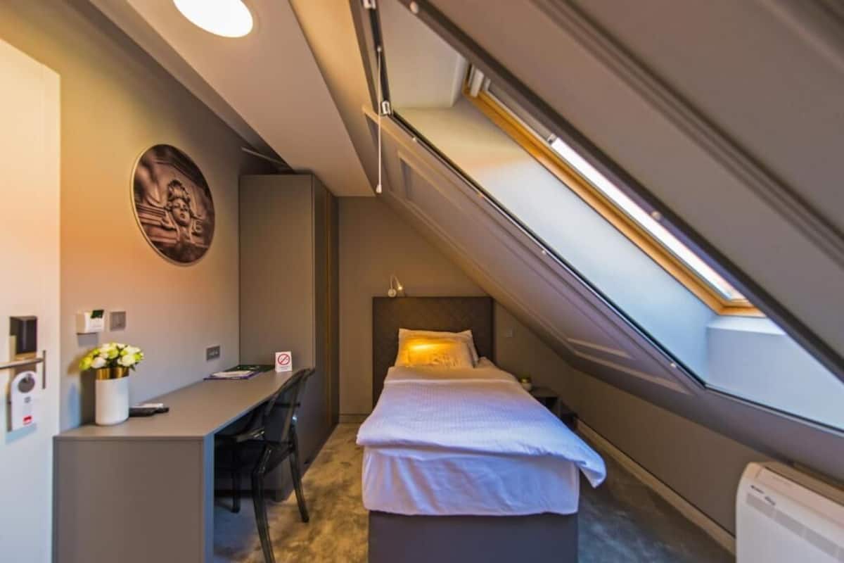 Ett kompakt hotellrum med en säng, ett skrivbord och en liten sittgrupp.