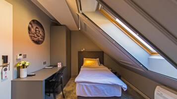 A compact hotel room with a bed, a desk, and a small seating area.