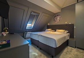 Un dormitorio con cama, un escritorio y una mesita. Se ve una ventana con vistas al exterior.