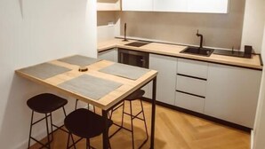 Une cuisine de taille réduite avec une table en bois, deux tabourets et un luminaire suspendu.