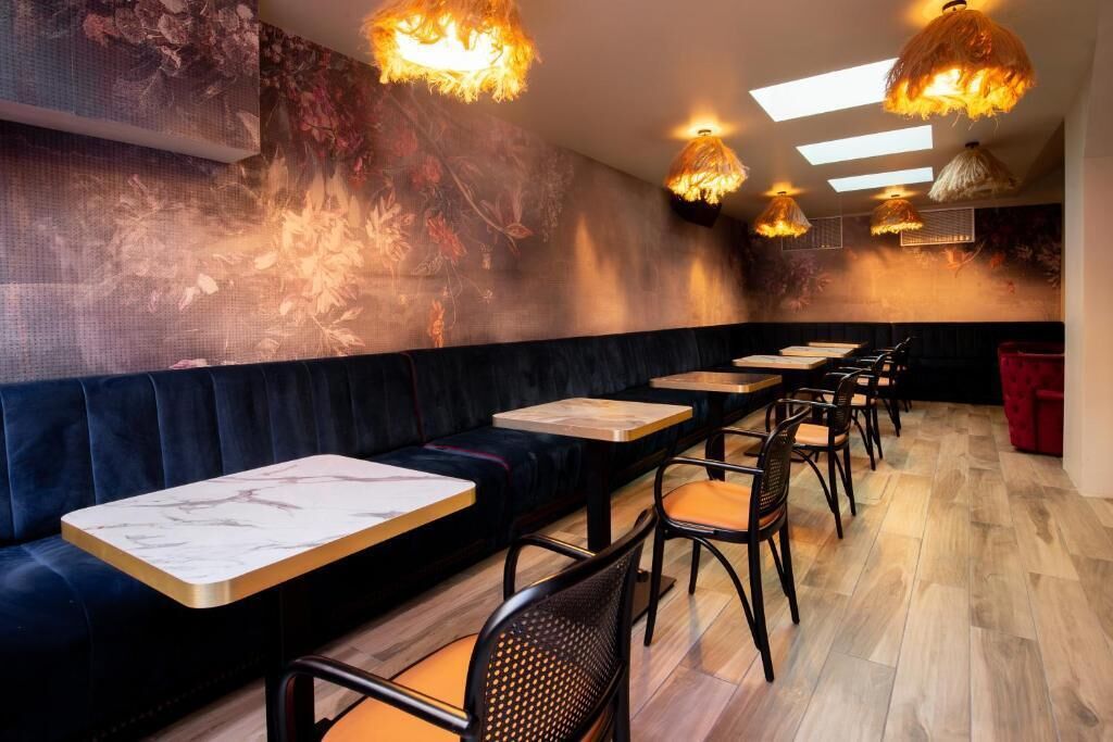 A restaurant with a long black cushioned bench, wooden tables, and chairs with orange cushions.