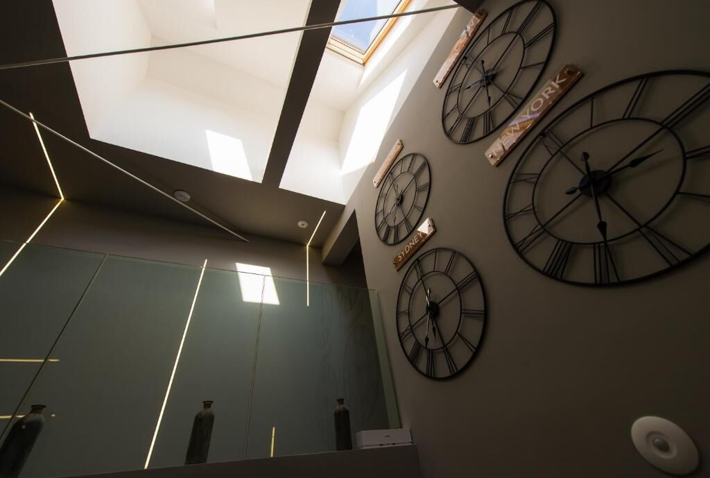 Un interior moderno con tragaluces, grandes relojes de pared y una superficie reflectante.