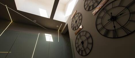 Un interior moderno con tragaluces, grandes relojes de pared y una superficie reflectante.