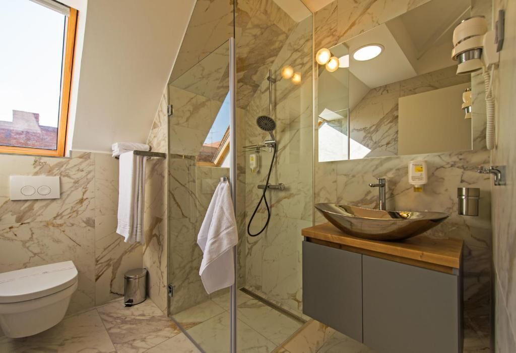 A modern bathroom with a glass-enclosed shower, a marble-tiled floor, a large mirror, and a wooden vanity with a bowl sink.