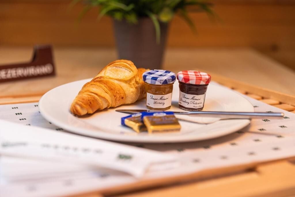 A croissant on a plate with two jars of honey and a knife.