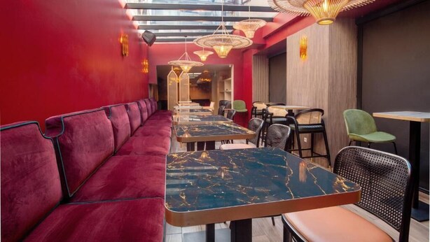 L’intérieur d’un restaurant moderne est agrémenté d’un banc recouvert d’un tissu rouge, de tables avec des plateaux en marbre noir et de chaises en osier.