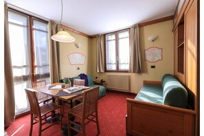 Une pièce chaleureuse avec une table en bois, des chaises, un canapé et une fenêtre avec des rideaux.