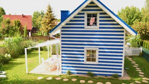 Ett hus med blå och vita ränder, en liten veranda och ett fönster.