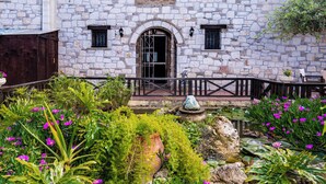 A stone building with a gated entrance, a small garden with pink flowers, and a pond with lily pads. - If you want to combine calmness and art , Arthouse is for you (ζακυνθος)