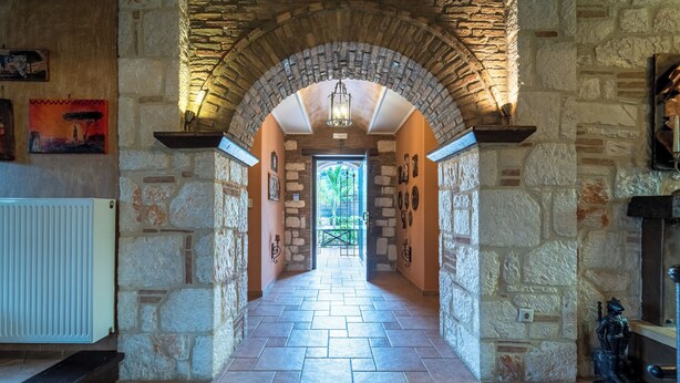 A stone-walled hallway with a tiled floor, leading to a door with a view of greenery outside. - If you want to combine calmness and art , Arthouse is for you (ζακυνθος)