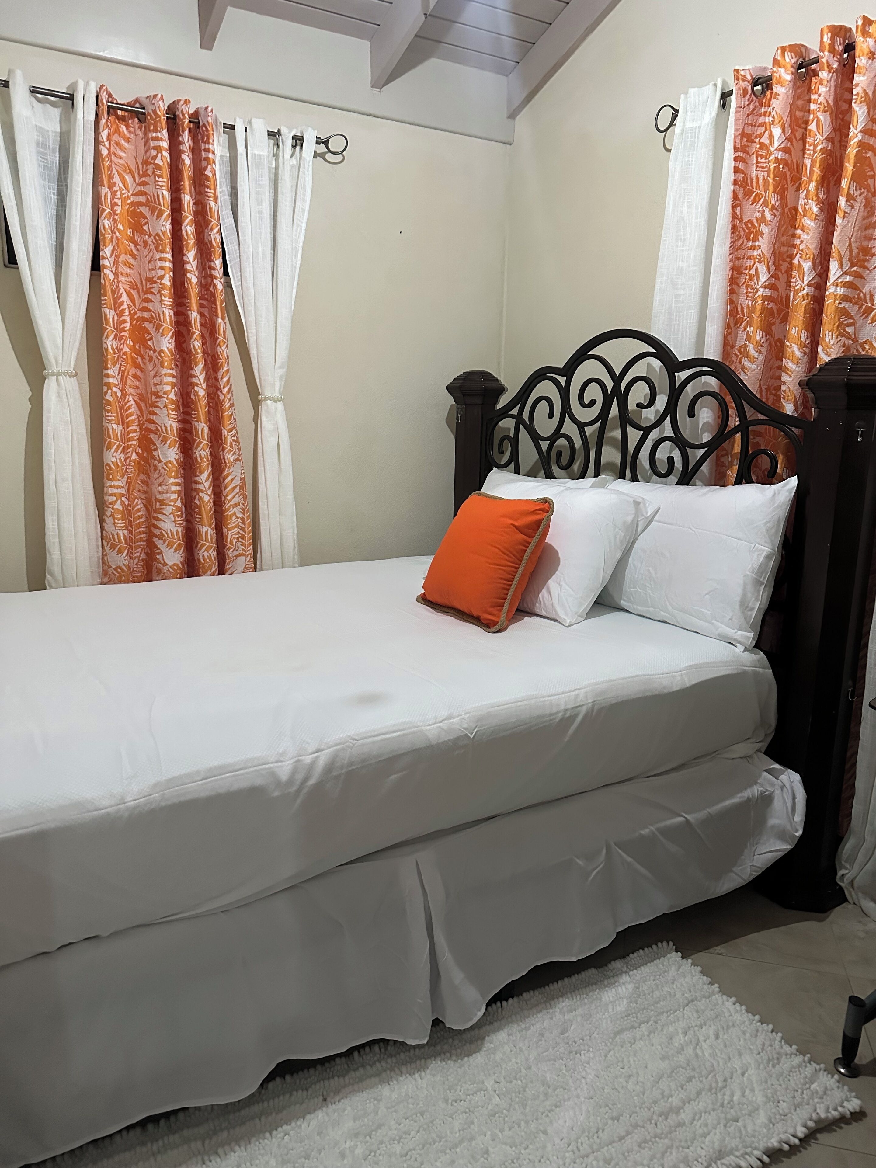 Een bed met witte beddengoed, een oranje kussen en een wit kussen.