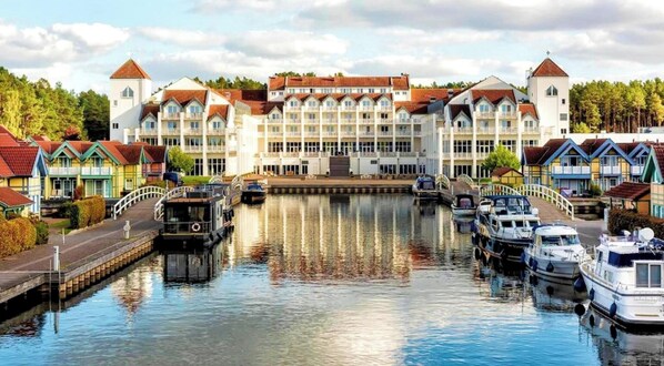 A canal with boats docked, a large building with multiple balconies, and colorful houses along the water.