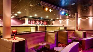 A modern bar area with cushioned seating, a bar counter, and overhead stage lighting.