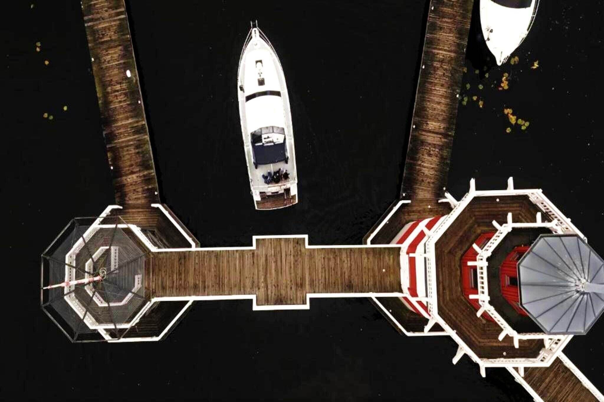 An aerial view of a dock with two boats, a wooden walkway, and a hexagonal structure with a central column.