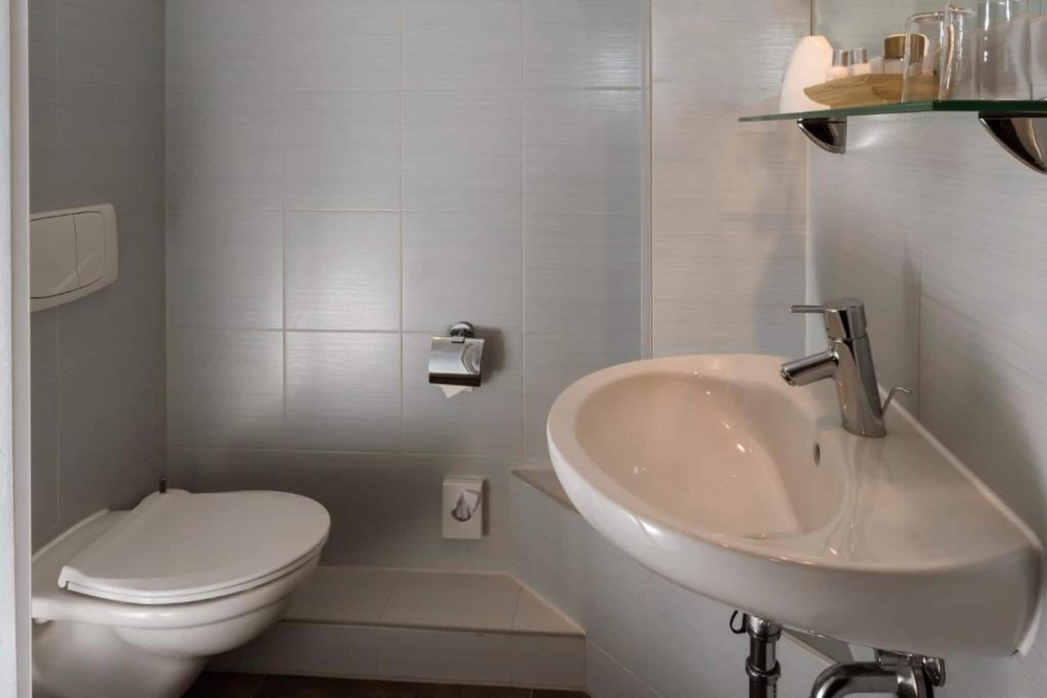 Un bagno con il water bianco, un lavandino e uno scaffale in vetro con articoli da toilette.