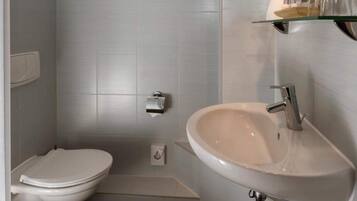 Un bagno con il water bianco, un lavandino e uno scaffale in vetro con articoli da toilette.