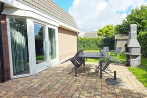 A patio with a table and chairs, a sliding glass door, and a chimney. - Pristine Beachside Base in Noordwijk (Noordwijk)
