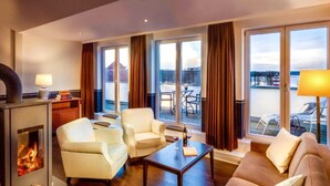 Quarto de hotel moderno com lareira, sofá, mesa de centro e varanda com vista para a água.