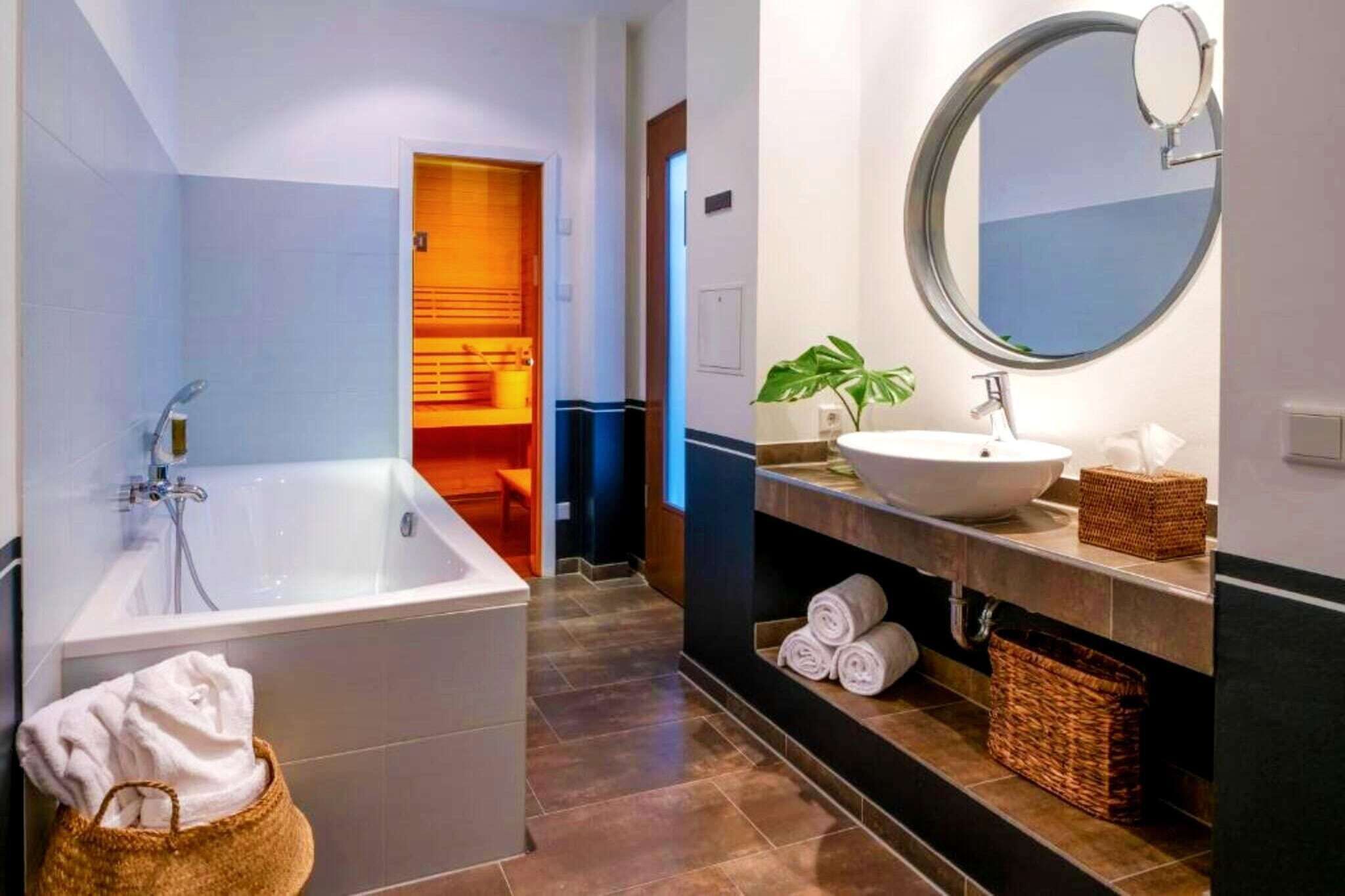 A modern bathroom with a large bathtub, a round mirror, a sink, and a towel rack.