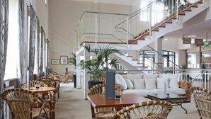 A spacious lobby with a high ceiling, a staircase, wicker furniture, and potted plants. - Sunday Resort Rügen Junior Suite Manor House (Sagard)