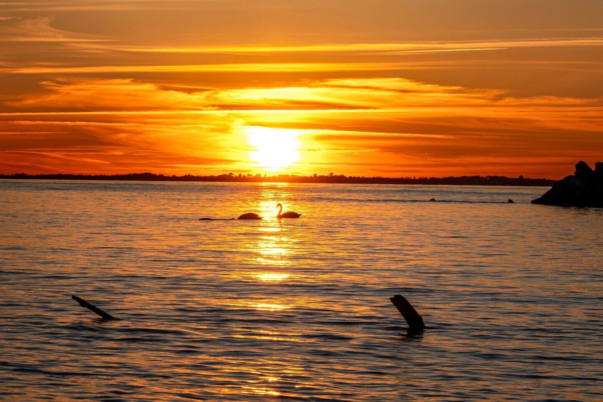 Solnedgang over et roligt vand med silhuetter af land og klipper i det fjerne.