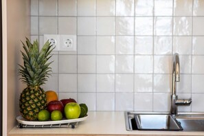 A kitchen counter with a fruit bowl containing a pineapple, apples, and limes. - Port View Apartment Aegina, Apartment (Aegina)