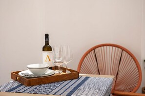 A dining setup with a bottle of wine, two glasses, and a tray with plates and cutlery. - Port View Apartment Aegina, Apartment (Aegina)