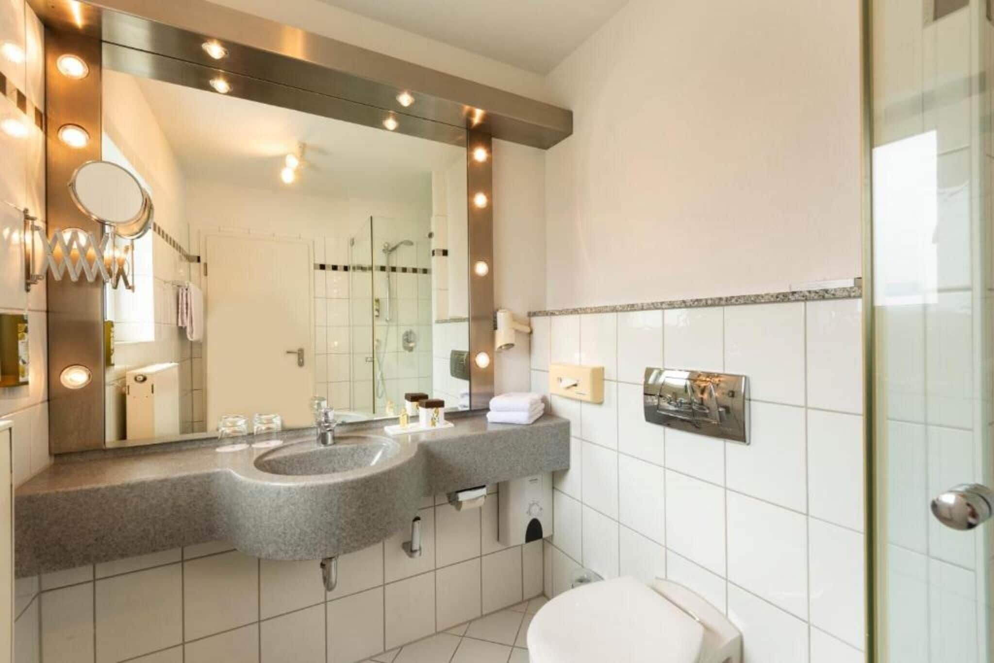 Un baño moderno con un espejo grande, dos lavamanos, un inodoro y una zona de ducha.